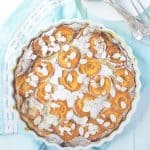 A round apricot clafoutis over a light blue background.