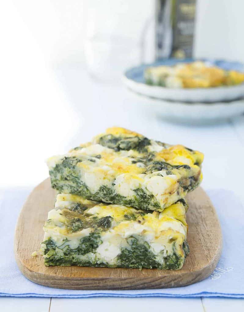 Two large slices of baked frittata with spinach and feta on a small wooden board.