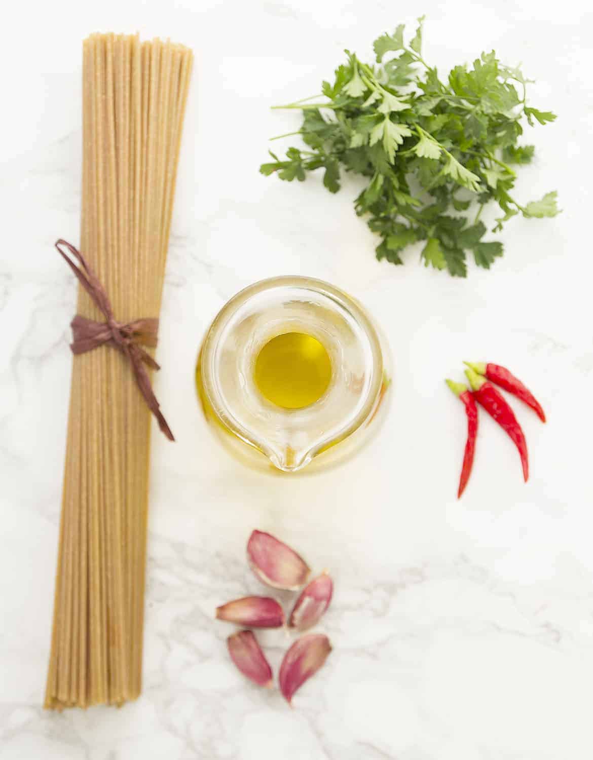 The ingredients for this pasta with garlic and olive oil are arranged on a white marble surface.