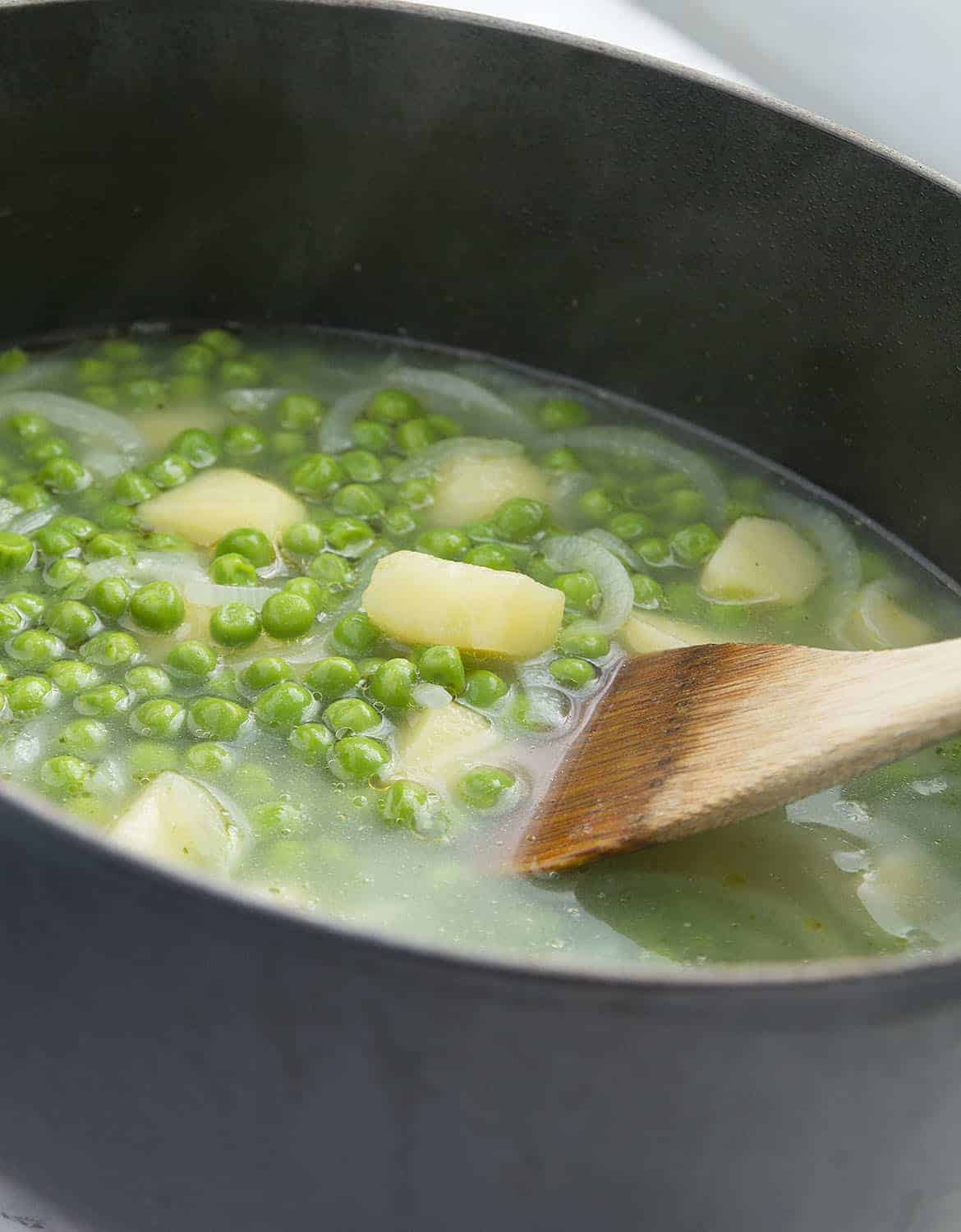 A black cast iron casserole full of pea soup with mint.