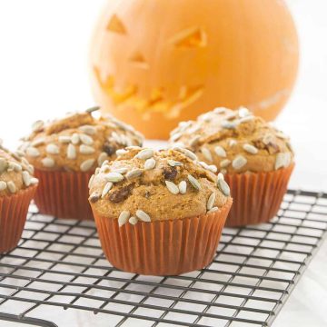 Blender pumpkin muffins on a cooling rack, a carved pumpkin in the background.