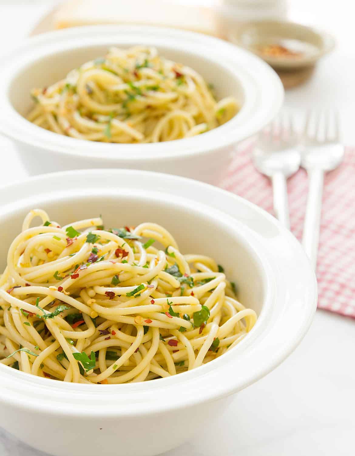 Two white bowls with garlic and olive oil spaghetti with chili flakes and chopped parsley- The Clever Meal