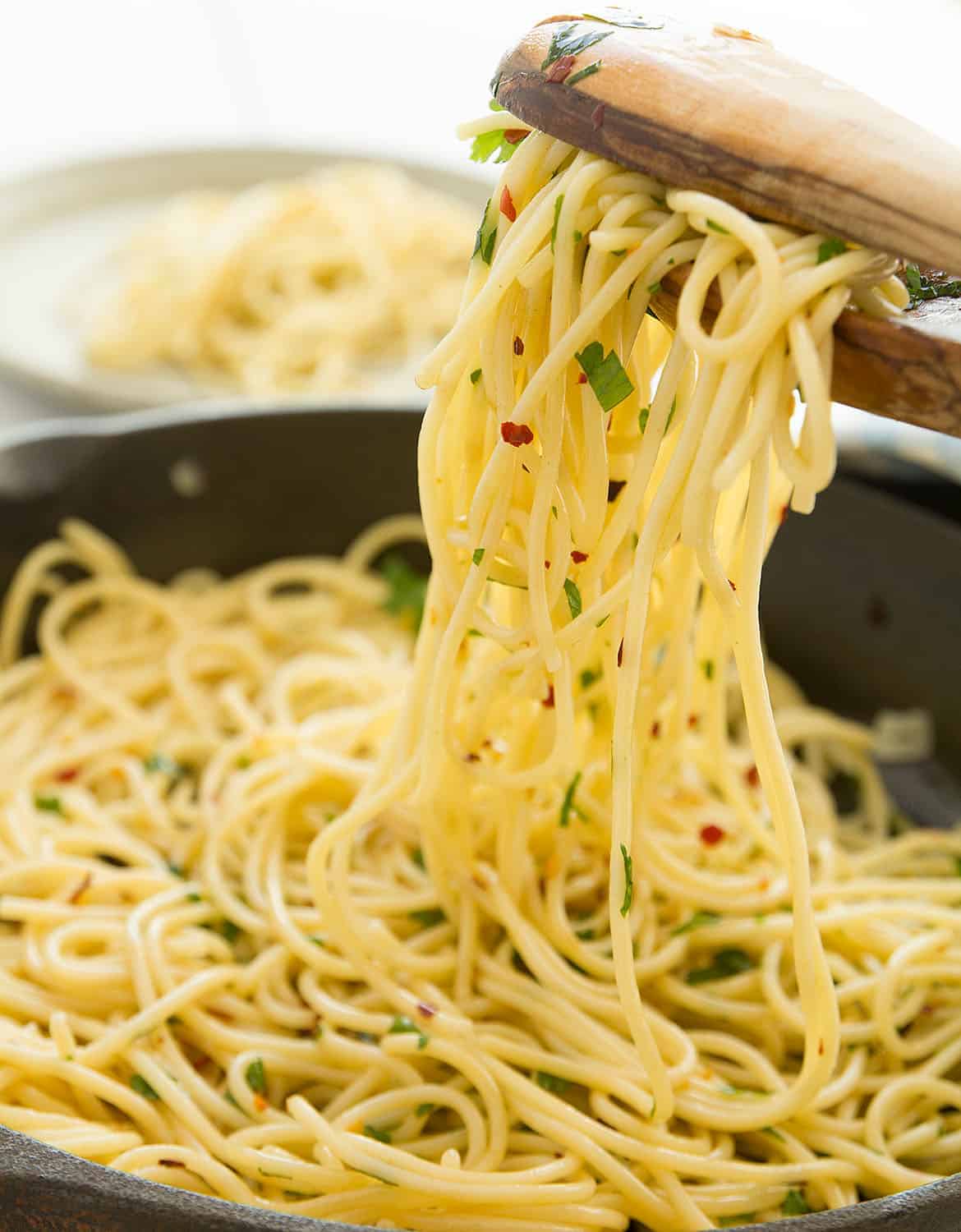 Two wooden spoons are lifting some pasta with garlic and olive oil.