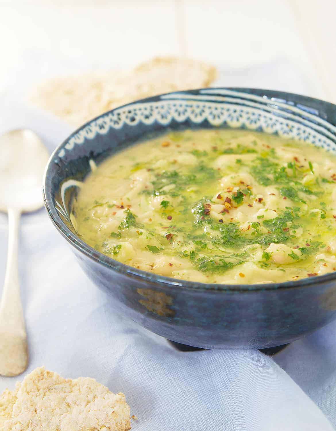 Thick white bean soup with parsley, chili flakes and olive oil in a blue bowl.