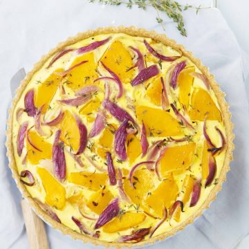 Top view of a round pumpkin quiche with slices of red onions.