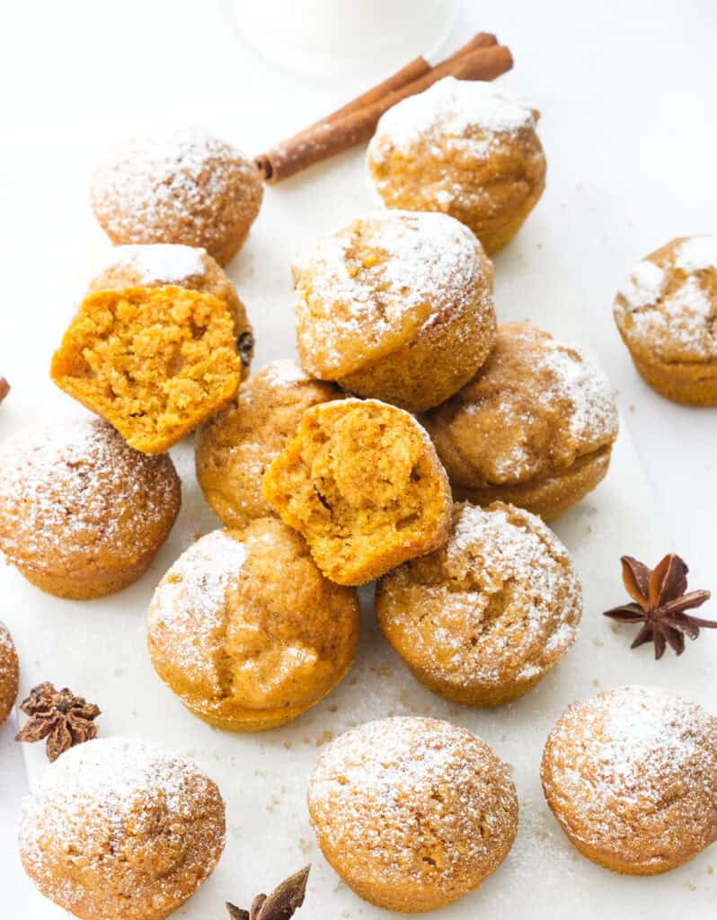 Many mini pumpkin muffins over a white background.