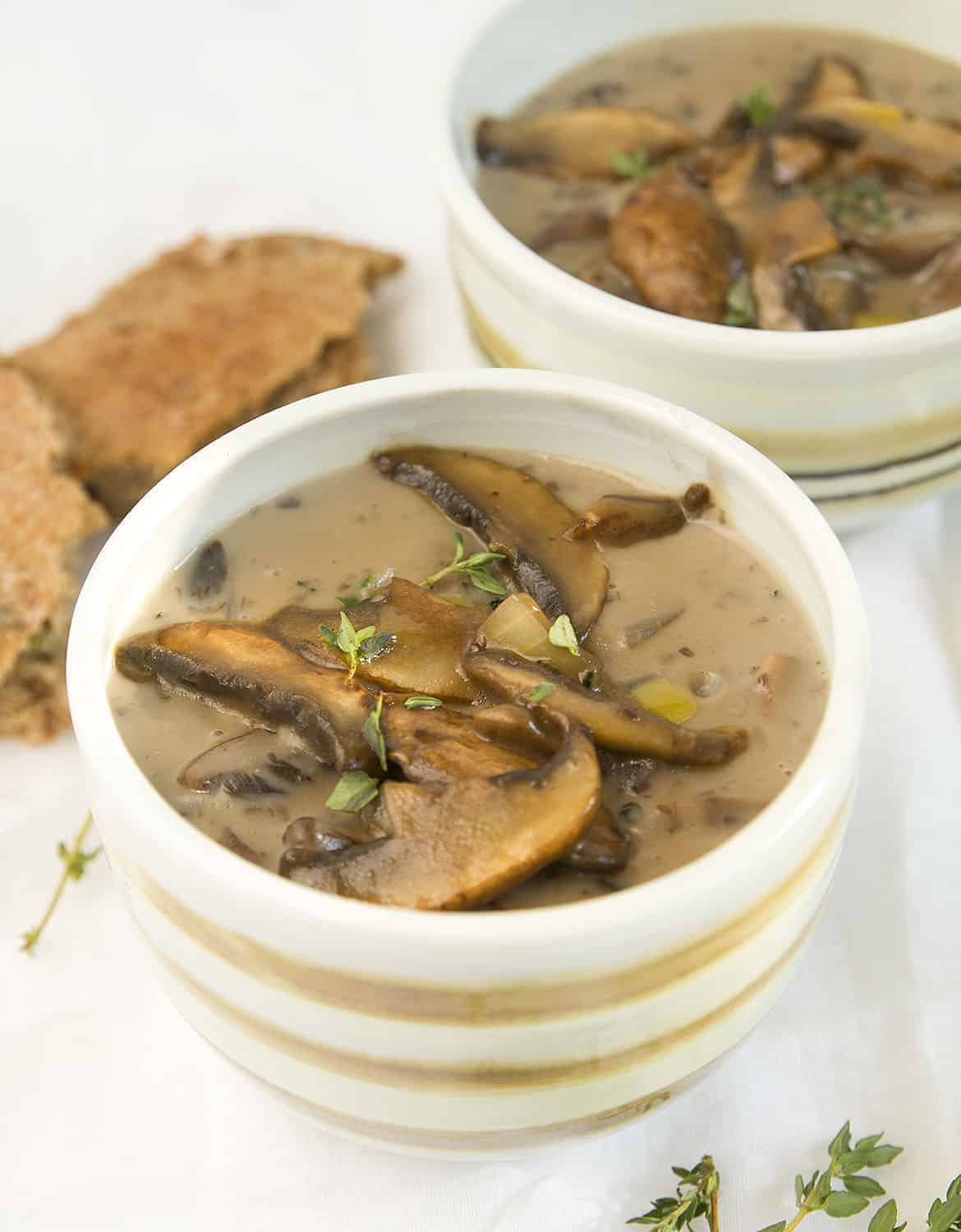 Two bowls full of healthy mushroom soups, two pieces of bread in the background.