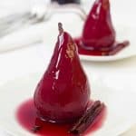 Two pears poached in red wine on two white plates.