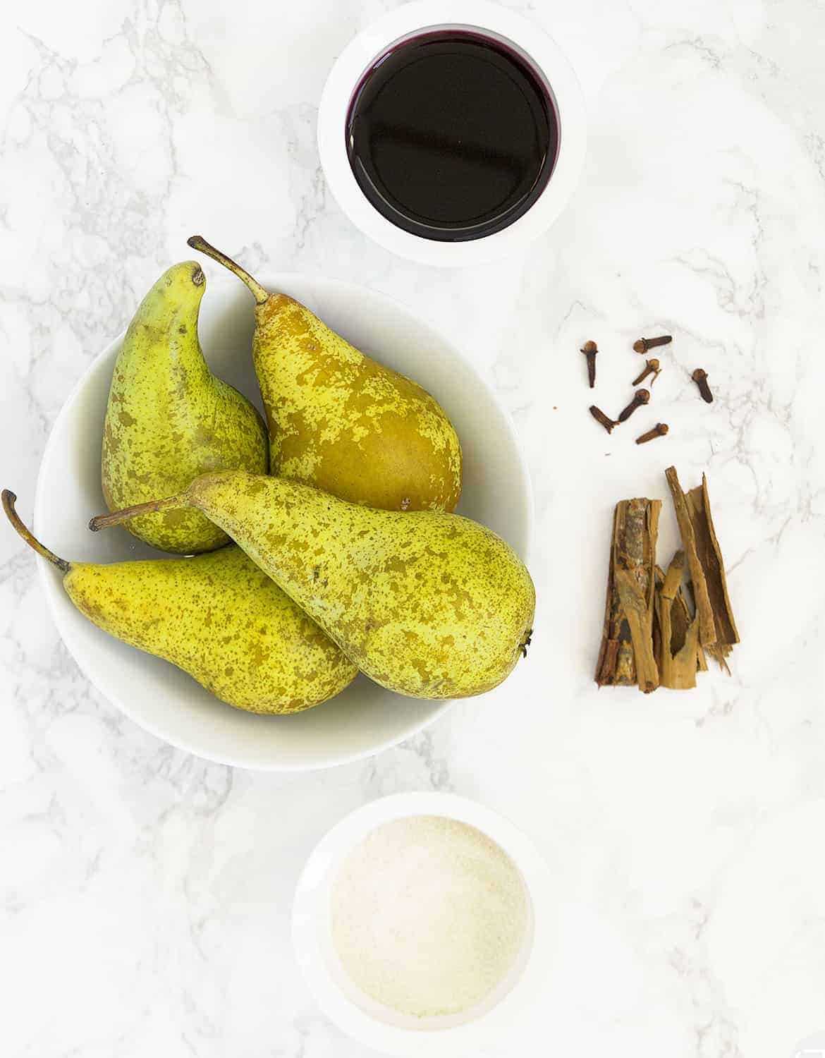 Red wine, sugar, cinnamon sticks and five green pears on a white bowl.