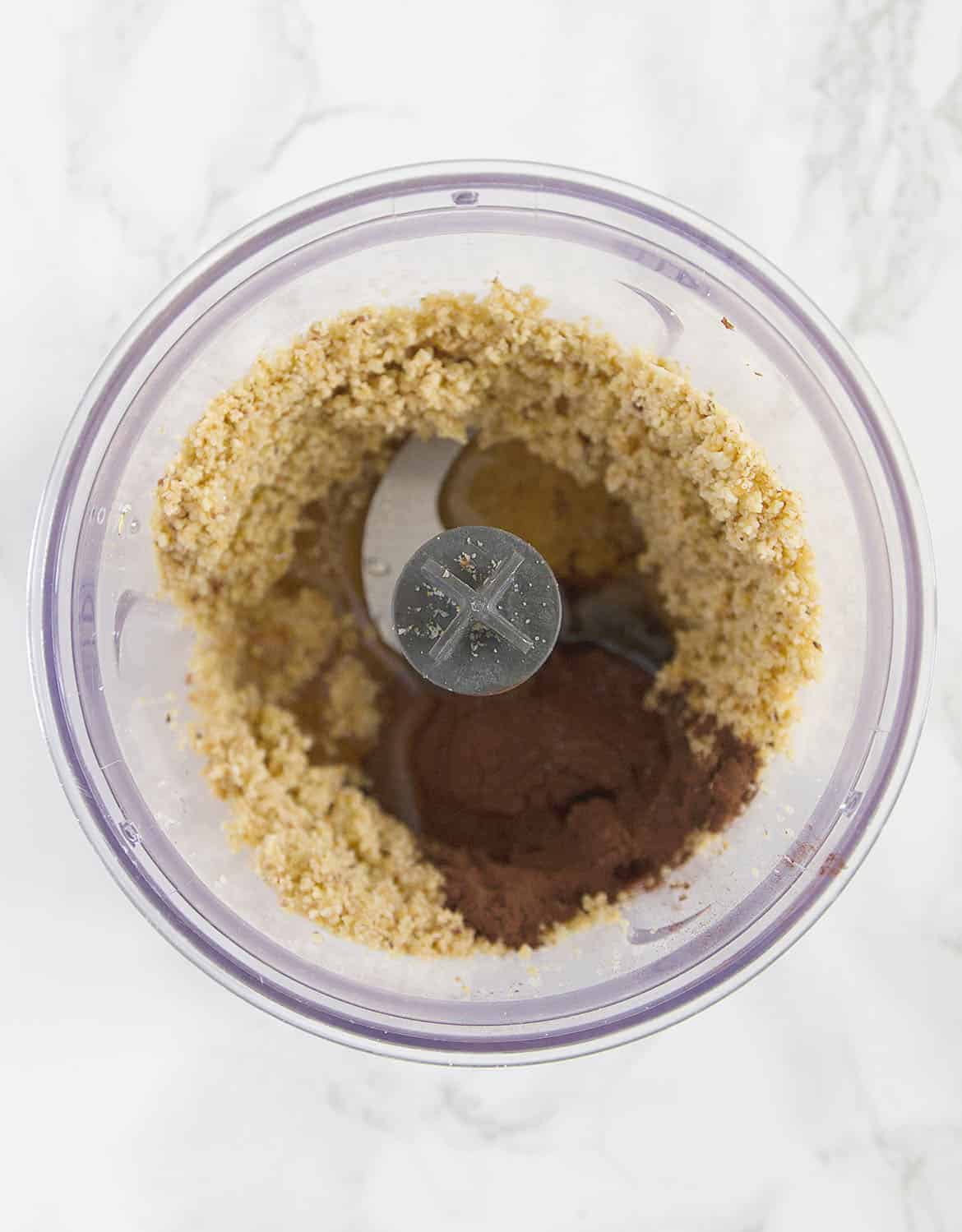Top view of a small food processor with ground hazelnuts and cocoa powder.