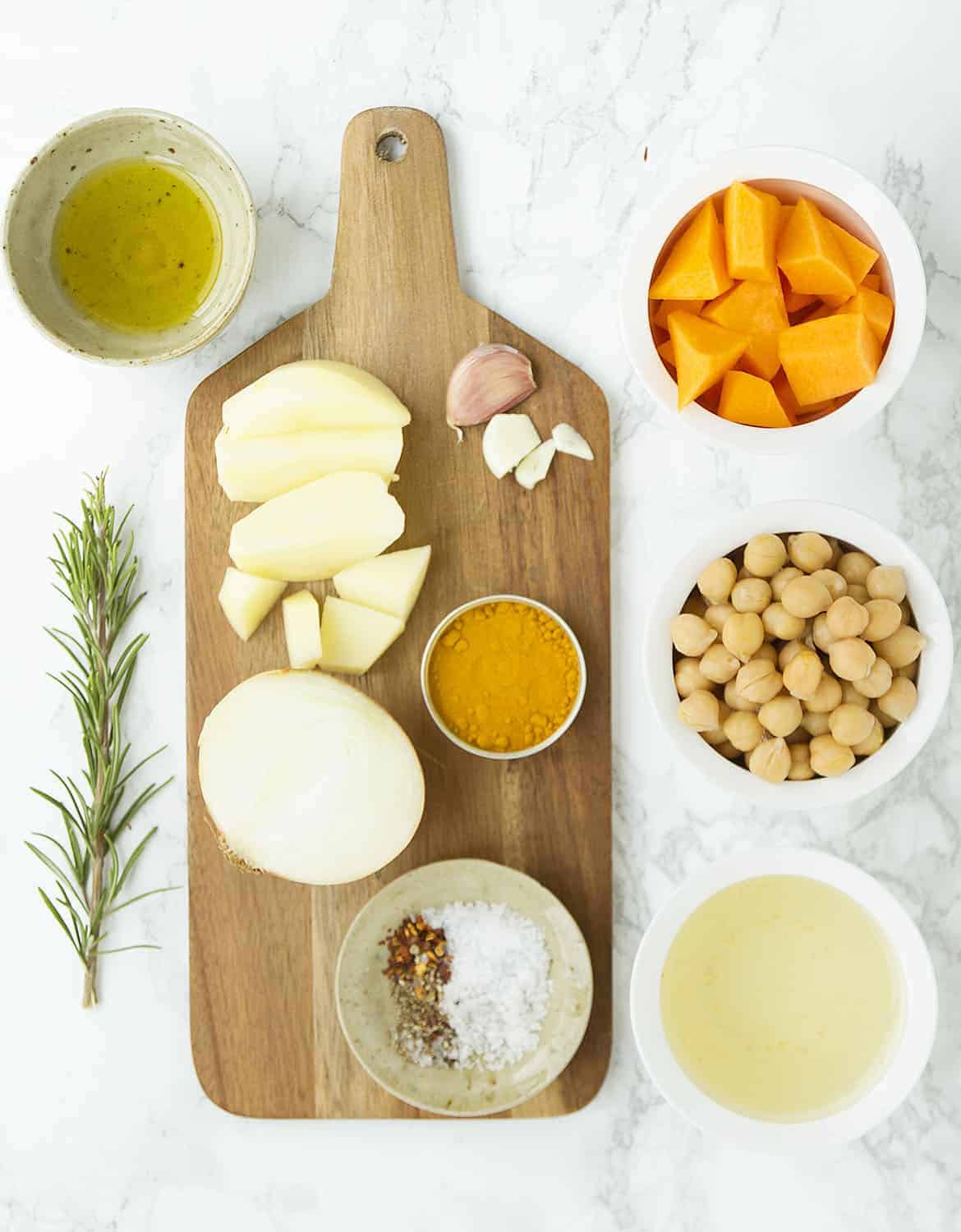 The ingredients for this butternut squash and chickpea soup are arranged on a white marble table.