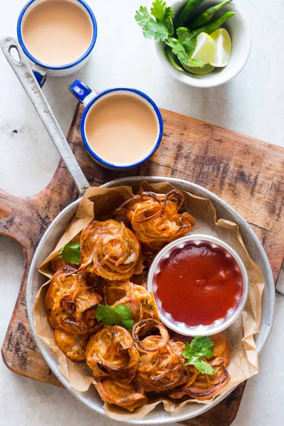 Crispy onions fritters on a skillet served with a red dipping sauce - My Food Story