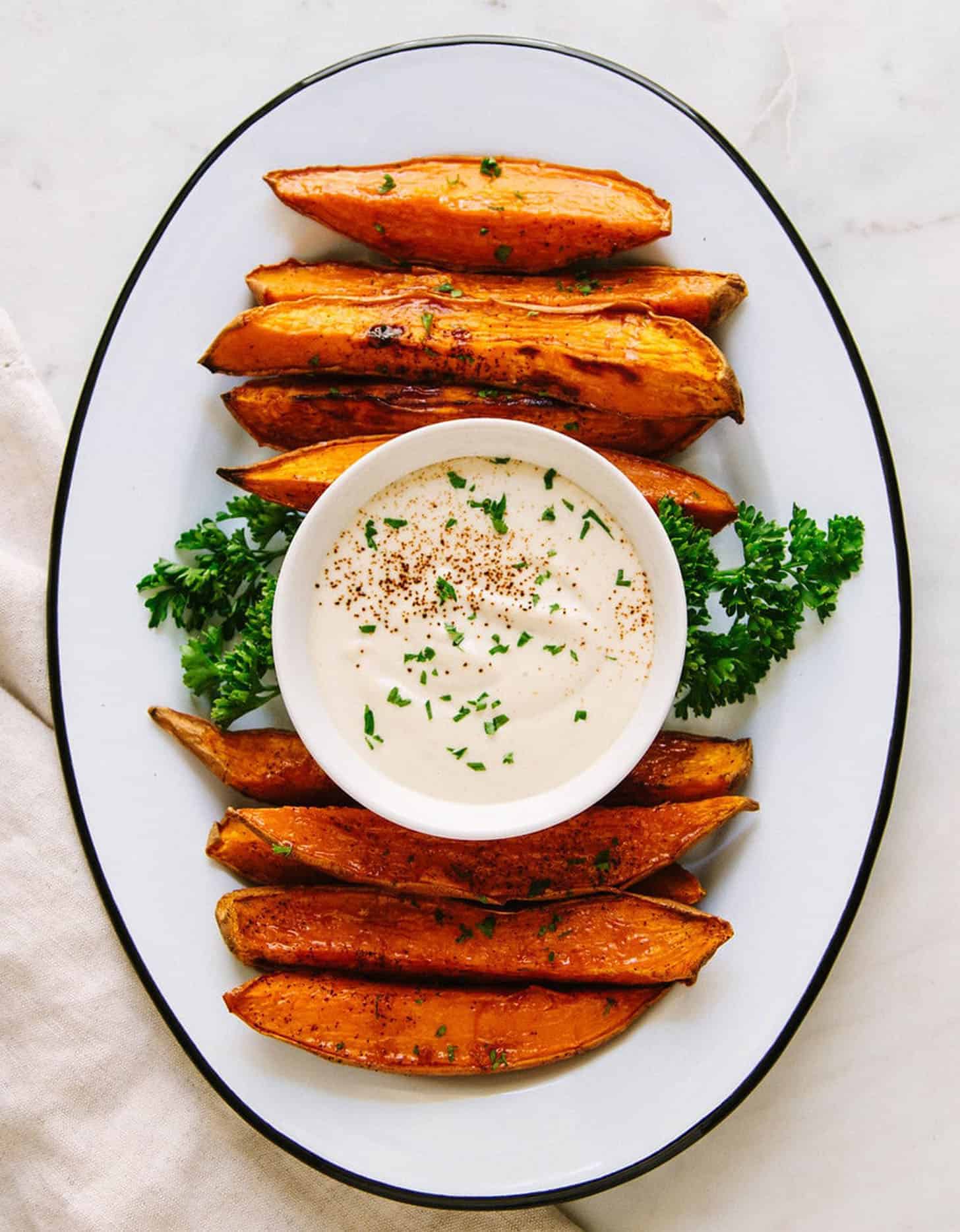 Baked potato wedges with dipping sauce on an oval white plate - by The Simple Veganista