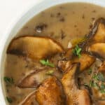 Close-up of a bowl full of mushroom soup over a white background.