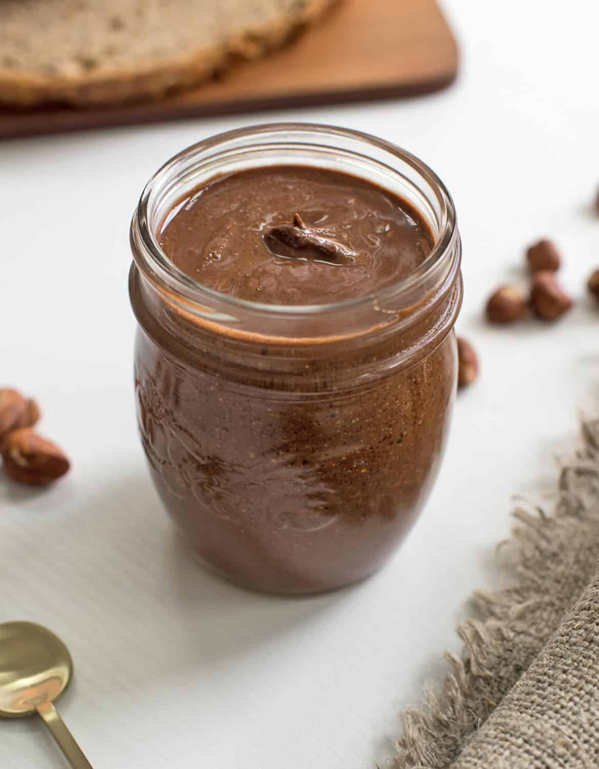 A glass jar full of VEGAN NUTELLA over a white background - Gathering Dreams