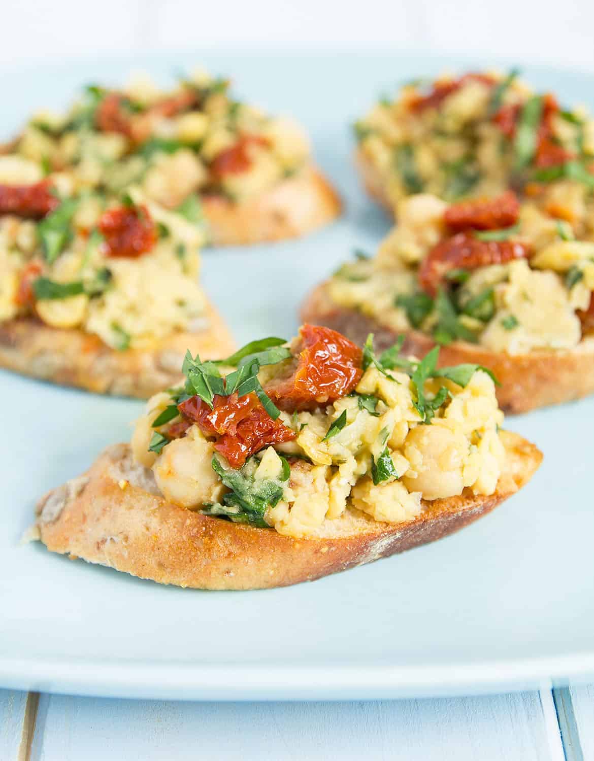 Chickpea bruschetta topped with sun dried tomatoes over a light blue plate - The Clever Meal