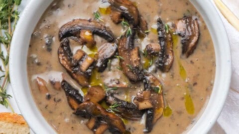 Top view of a white bowl full of mushroom soup without cream served with bread.