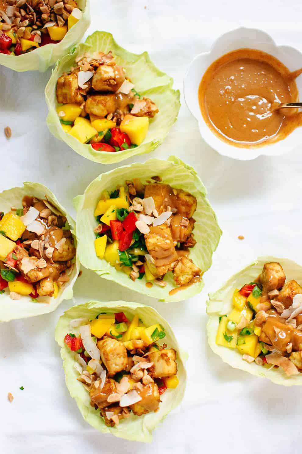 Six Mango Cabbage Wraps with Tofu and Peanut Sauce on white parchment paper - Cookie+Katie: