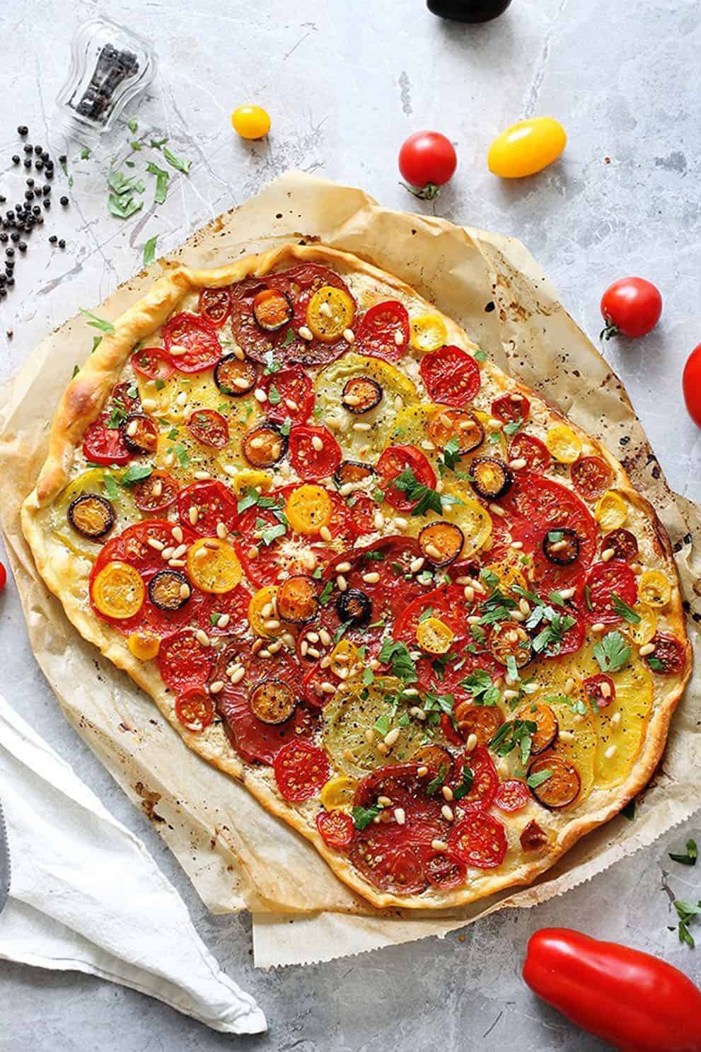 Vegan tomato flatbread on parchment paper over a grey background - Green Evi