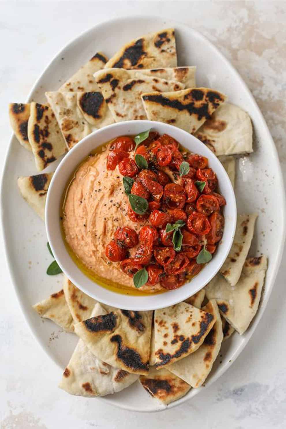 Tomato hummus in a white bowl served with grilled pita bread - How Sweet Eats