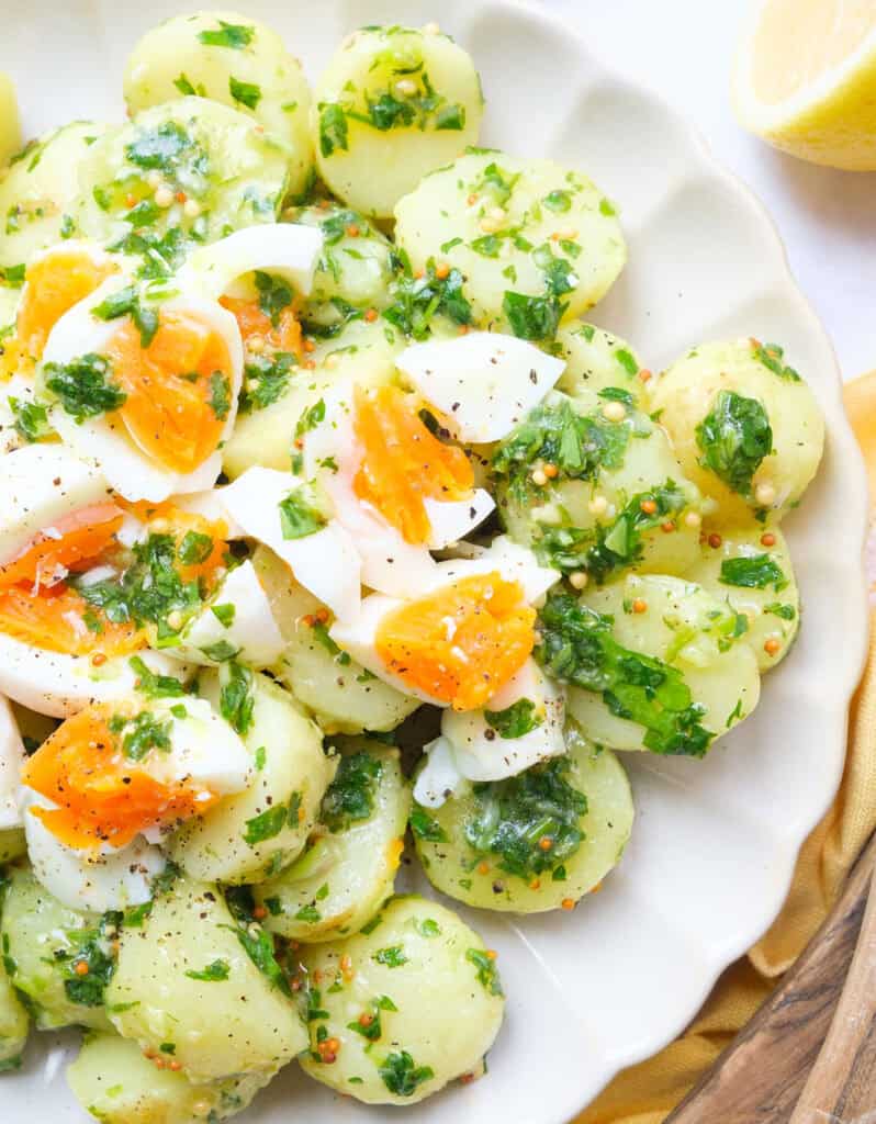 Top view of potato egg salad with parsley served on a white plate.