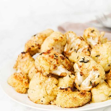Roasted balsamic cauliflower florets on a plate over a white background.