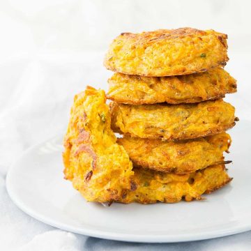 A pile of butternut squash fritters on a plate over a white background.