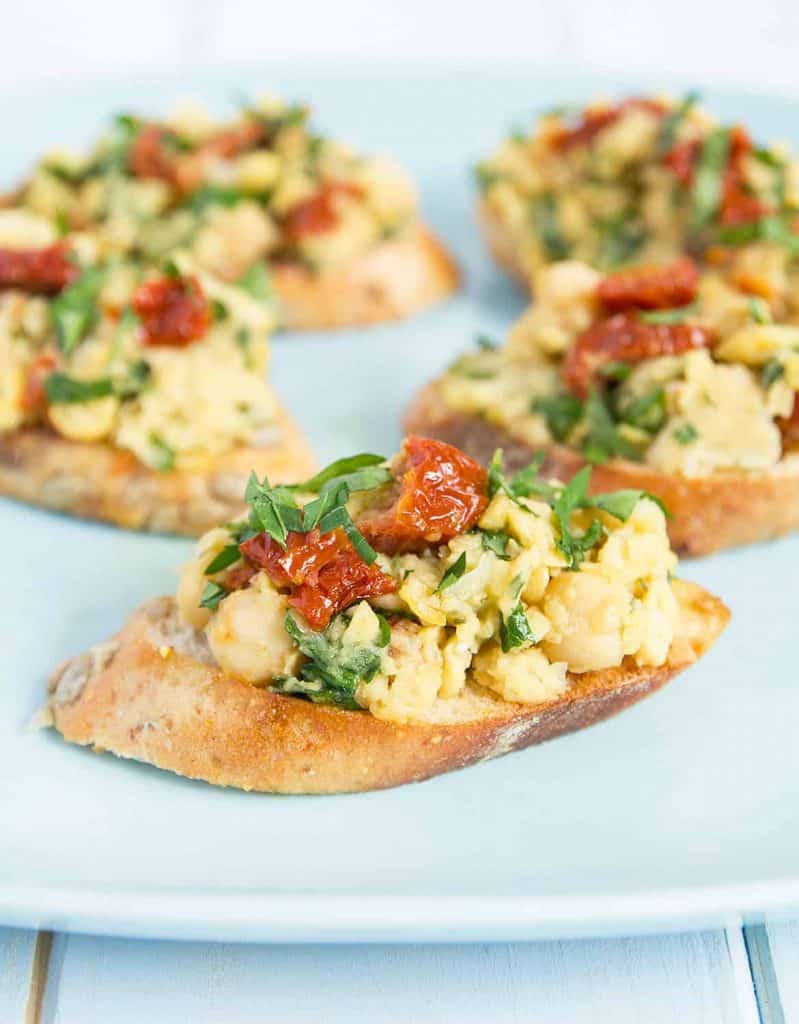 Chickpea bruschetta with sun dried tomatoes over a light blue plate.