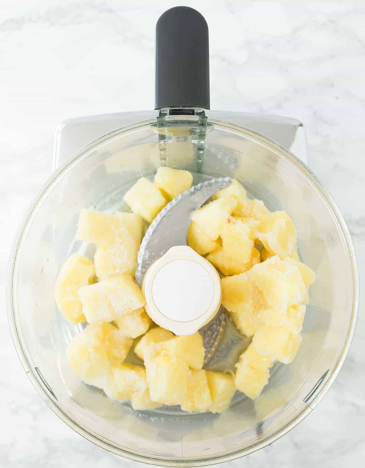 A food processor bowl with frozen pineapple chunks.