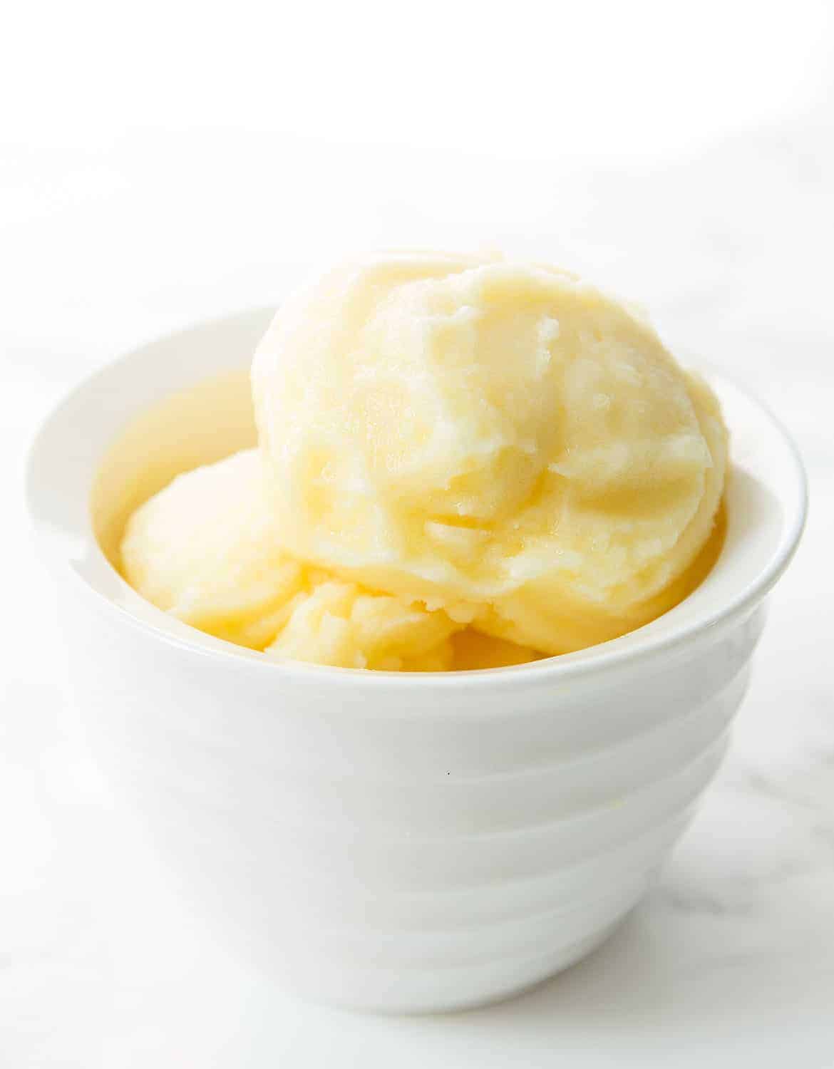 Pineapple sorbet in a white bowl over a white background.