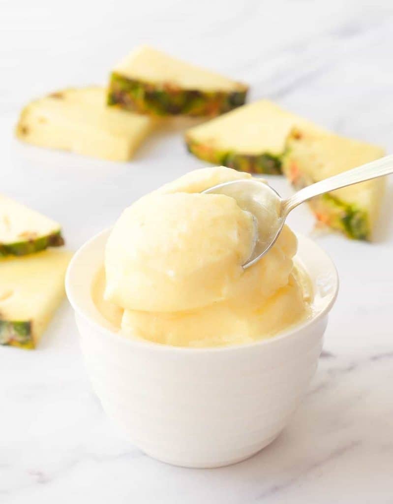 Pineapple sorbet with a spoon over a white background.