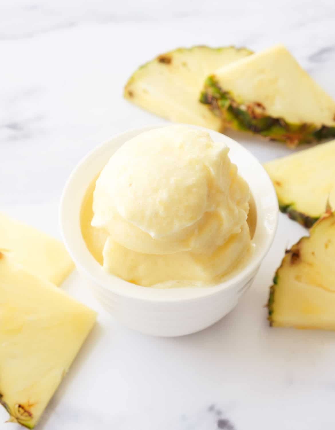 Pineapple sorbet in a white bowl over a white background.