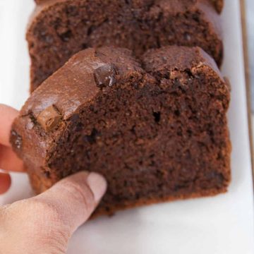 A hand is grabbing the first slice of a chocolate zucchini bread.