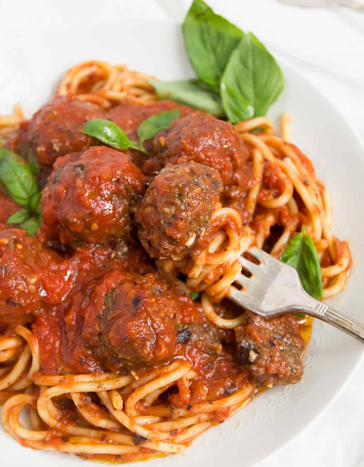 Vegan meatballs with green basil leaves and spaghetti on a white plate.