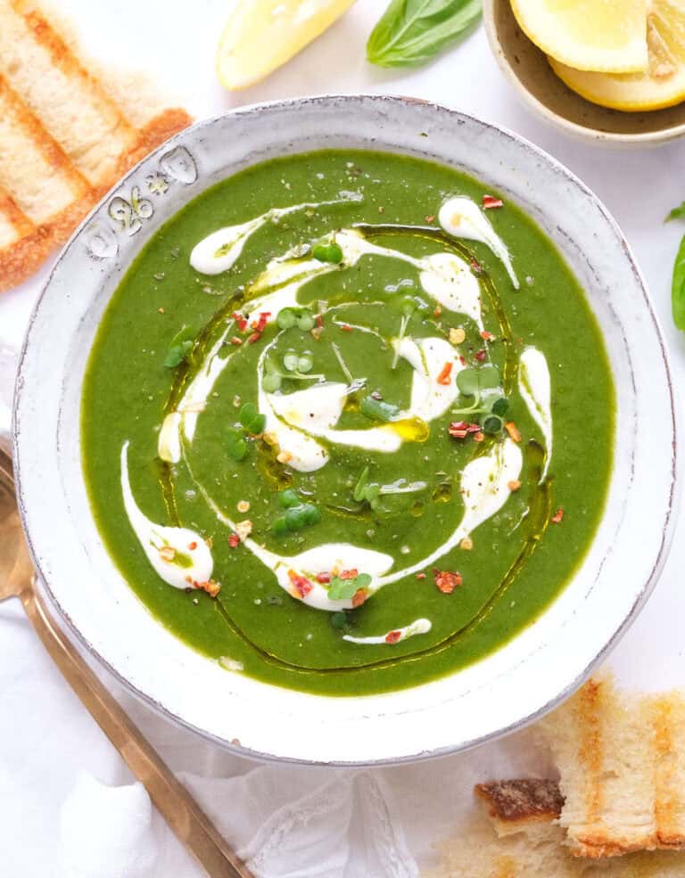 Top view of a white bowl full of creamy spinach soup topped with some dots of white yogurt.