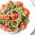 Italian tomato and cucumber salad with red onion rings on a white plate.