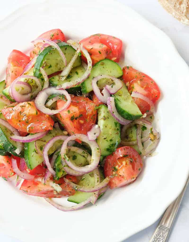 Italian tomato and cucumber salad with red onion rings on a white plate.
