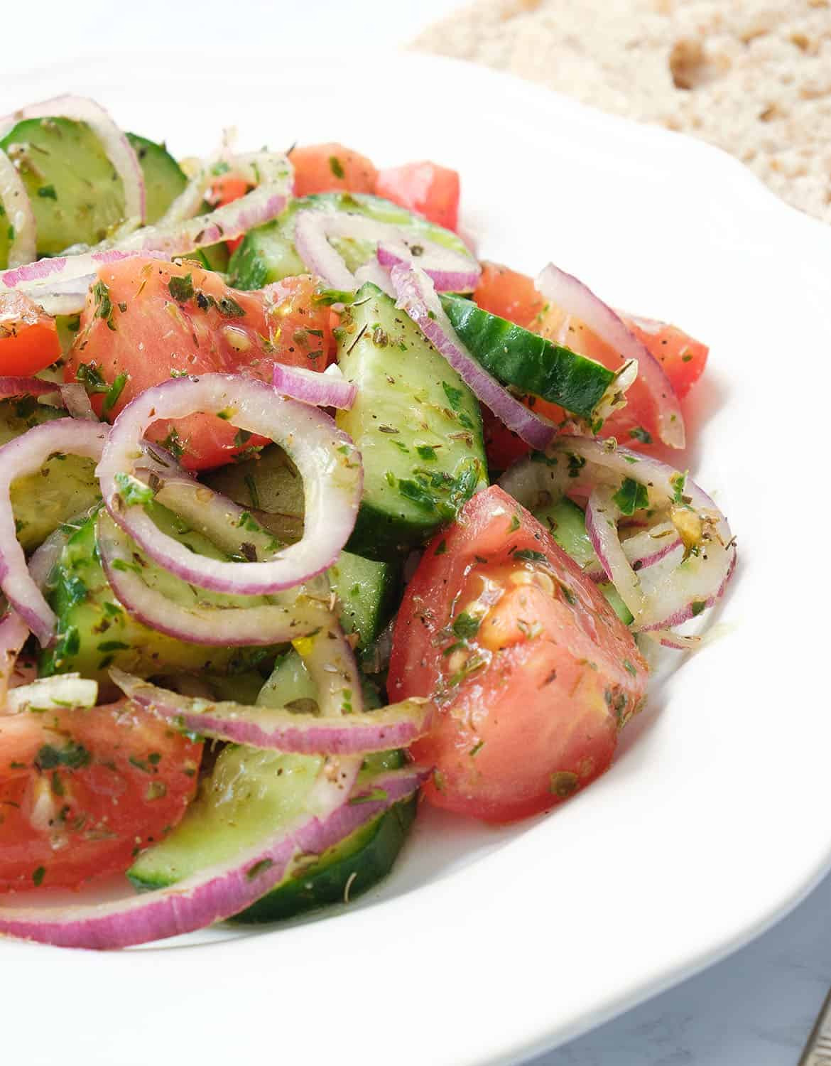 Tomato and cucumber salad with onion rings on a white plate.