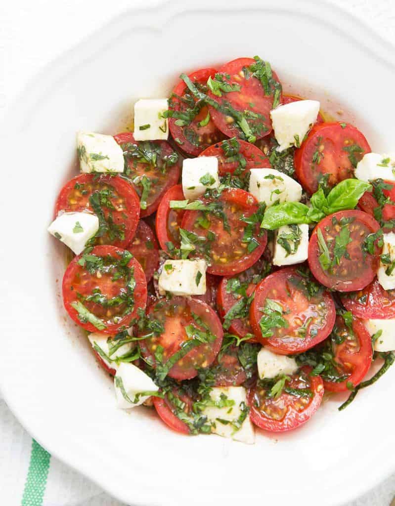 Marinated tomato and mozzarella salad with fresh herbs on a white plate.