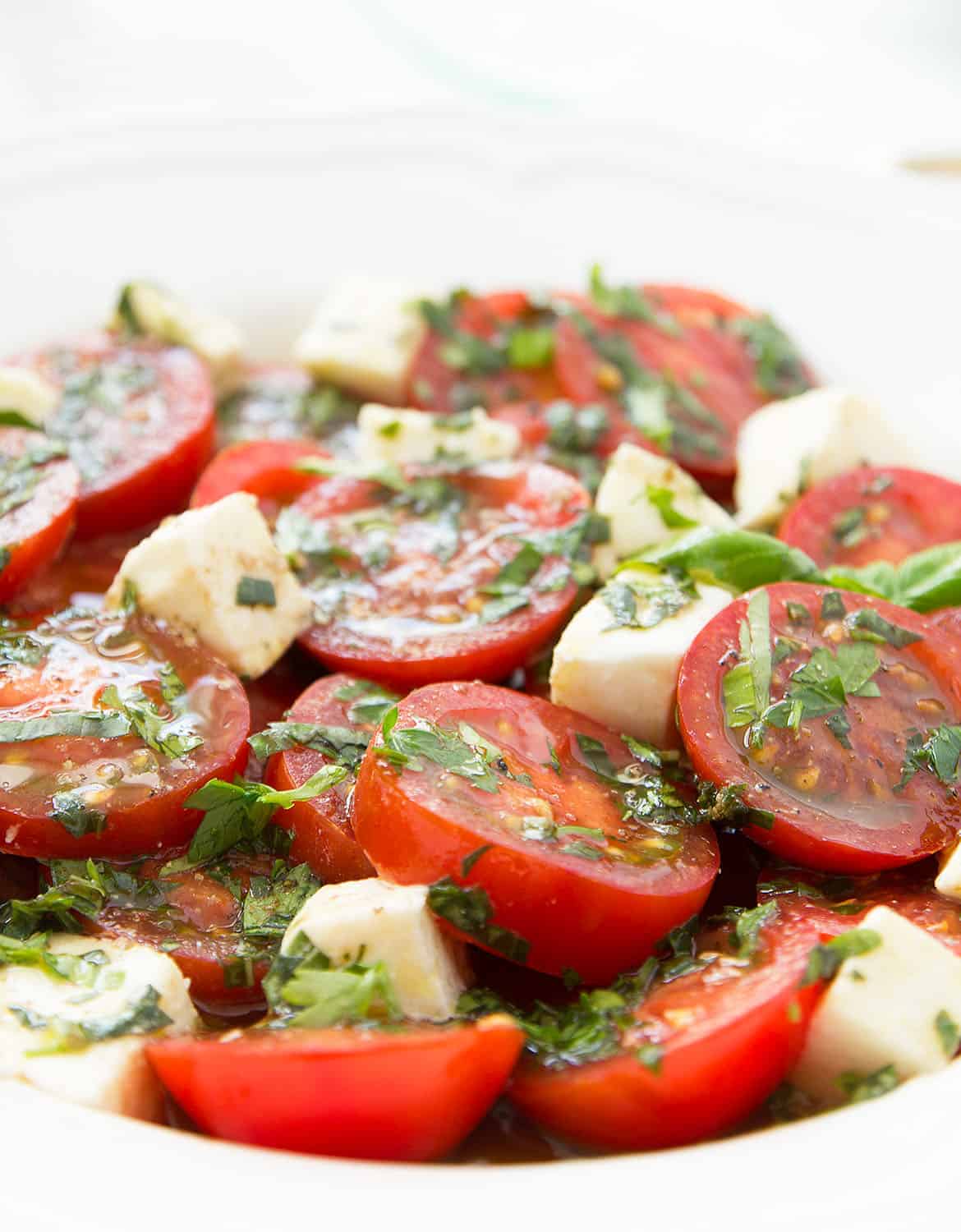 Marinated tomato salad on a white plate over a total white background.