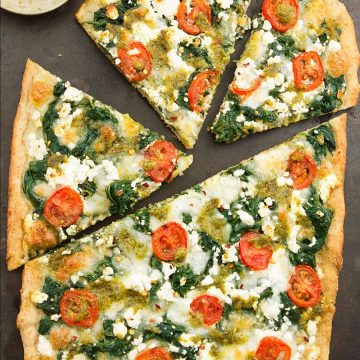 Top view of spinach pizza with feta and cherry tomatoes over a black background.