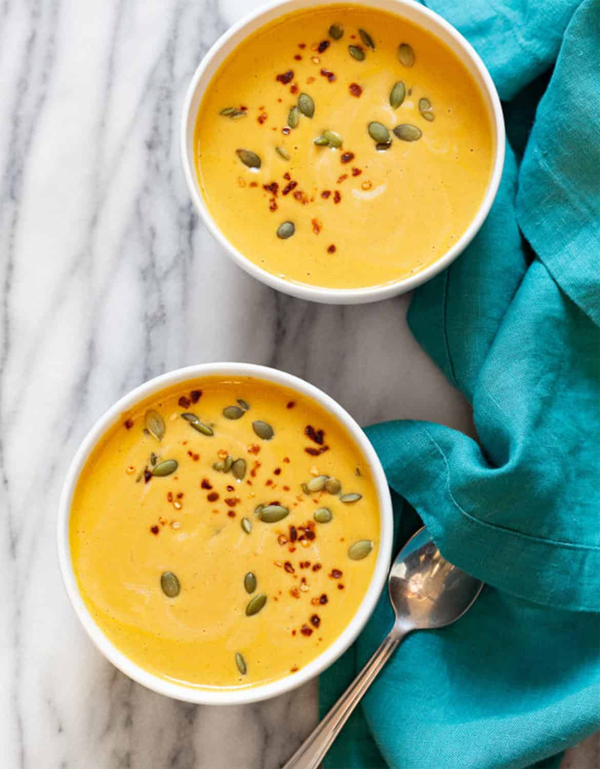 Two white bowls full of vegan pumpkin soup with a blue tea towel in the background - Vegan Richa