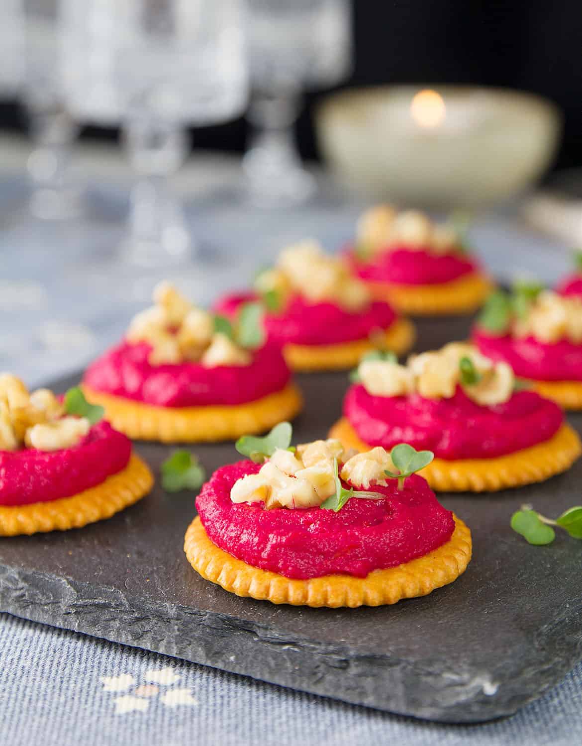 Small round crackers topped with beetroot hummus and chopped walnuts over a black background.