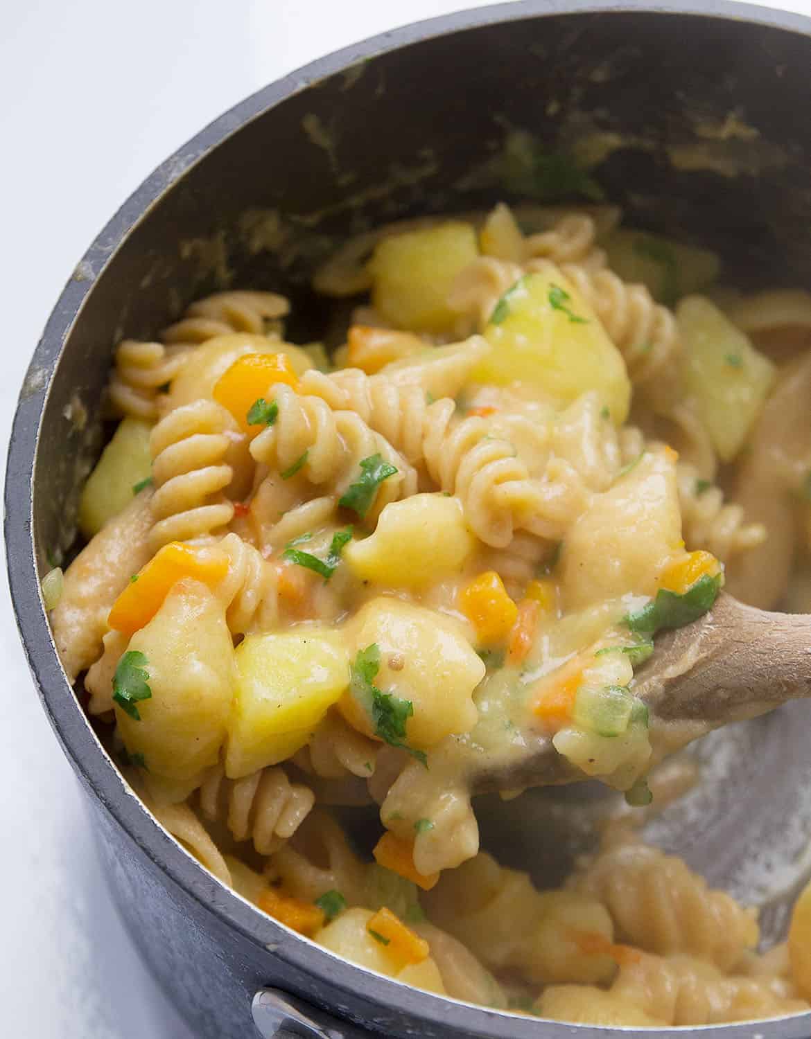 A wooden spoon stirs a creamy potato pasta inside a black pot.