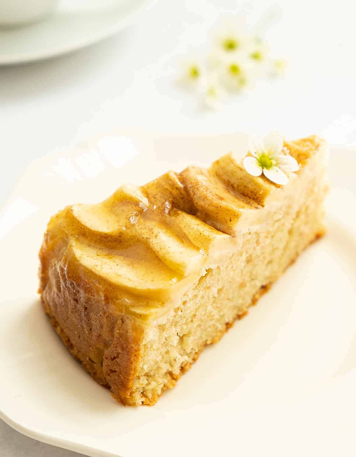 A slice of apple cake decorated with a small white flower on a white plate.