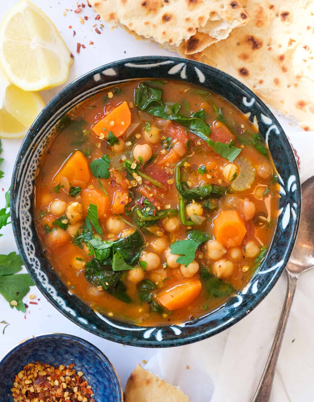 Top view of a dark bowl full of Mediterranean soup with chickpeas, veggies and spinach.