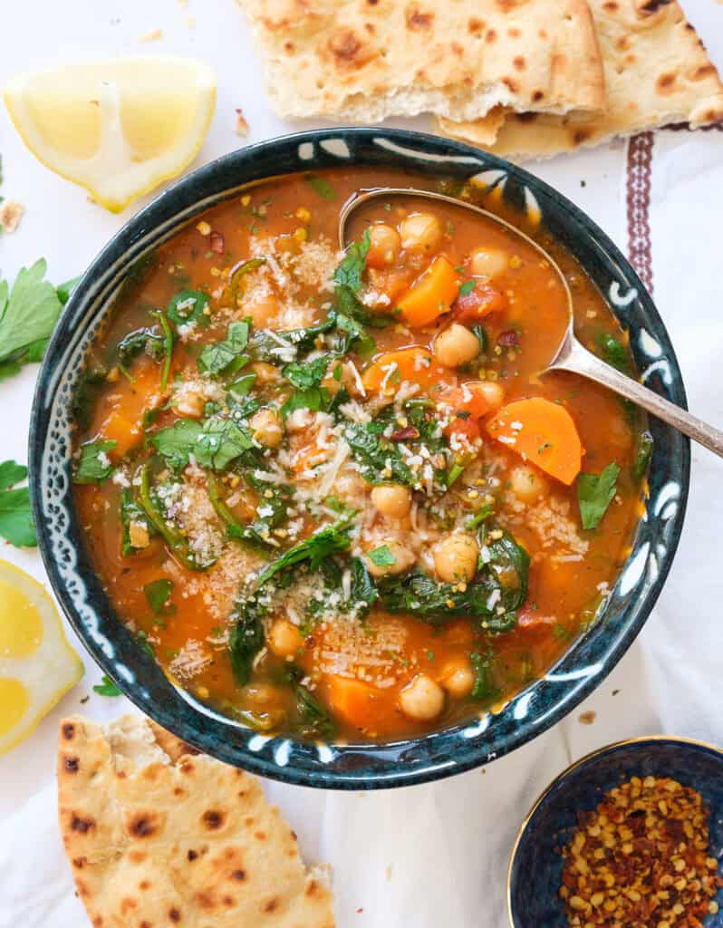 Top view of a bowl full of Mediterranean soup with chickpeas, veggies, spinach and topped with parmesan.