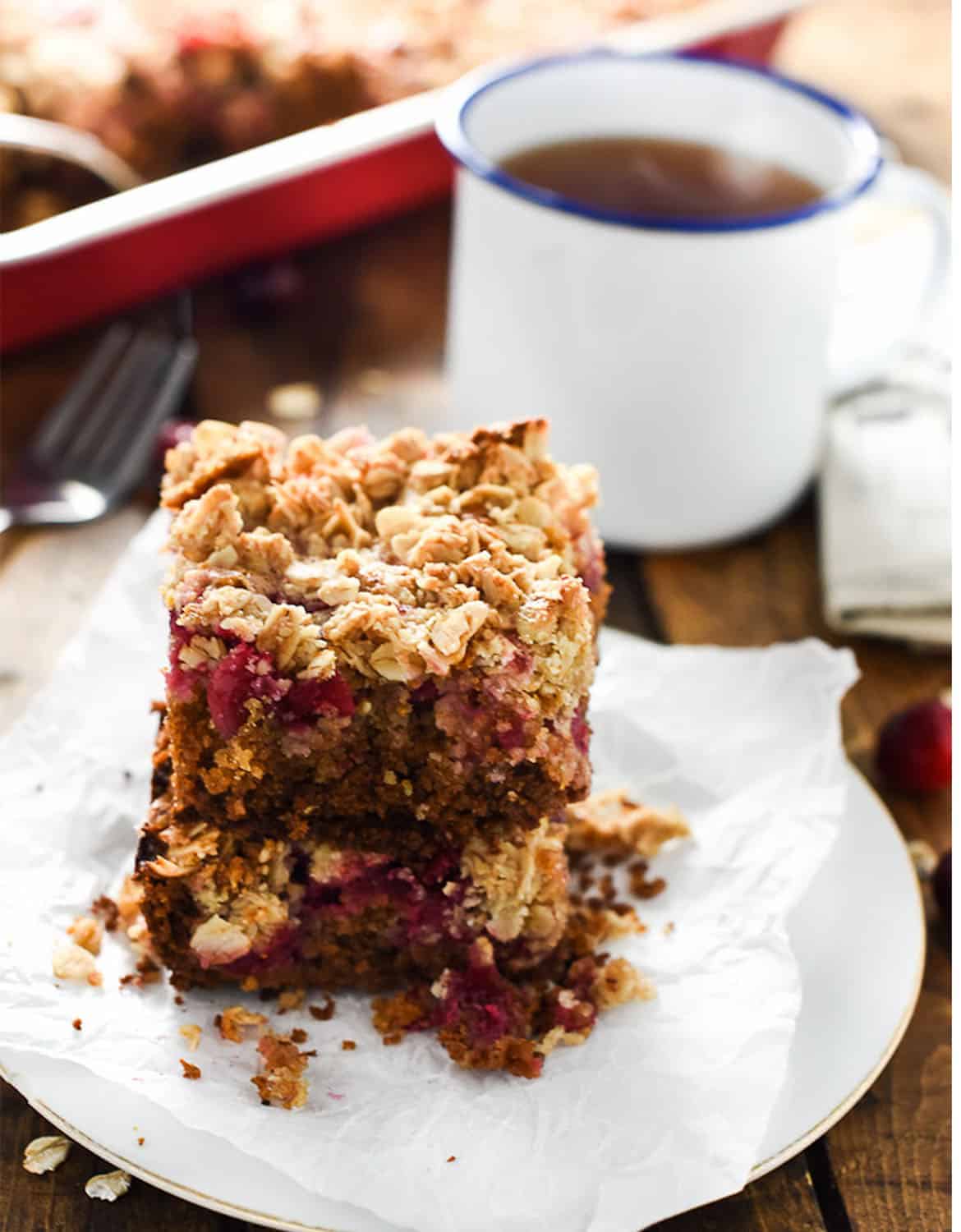 The healthy cranberry coffee cake is on a white napkin with a cup of tea in the background - The Endless Meal