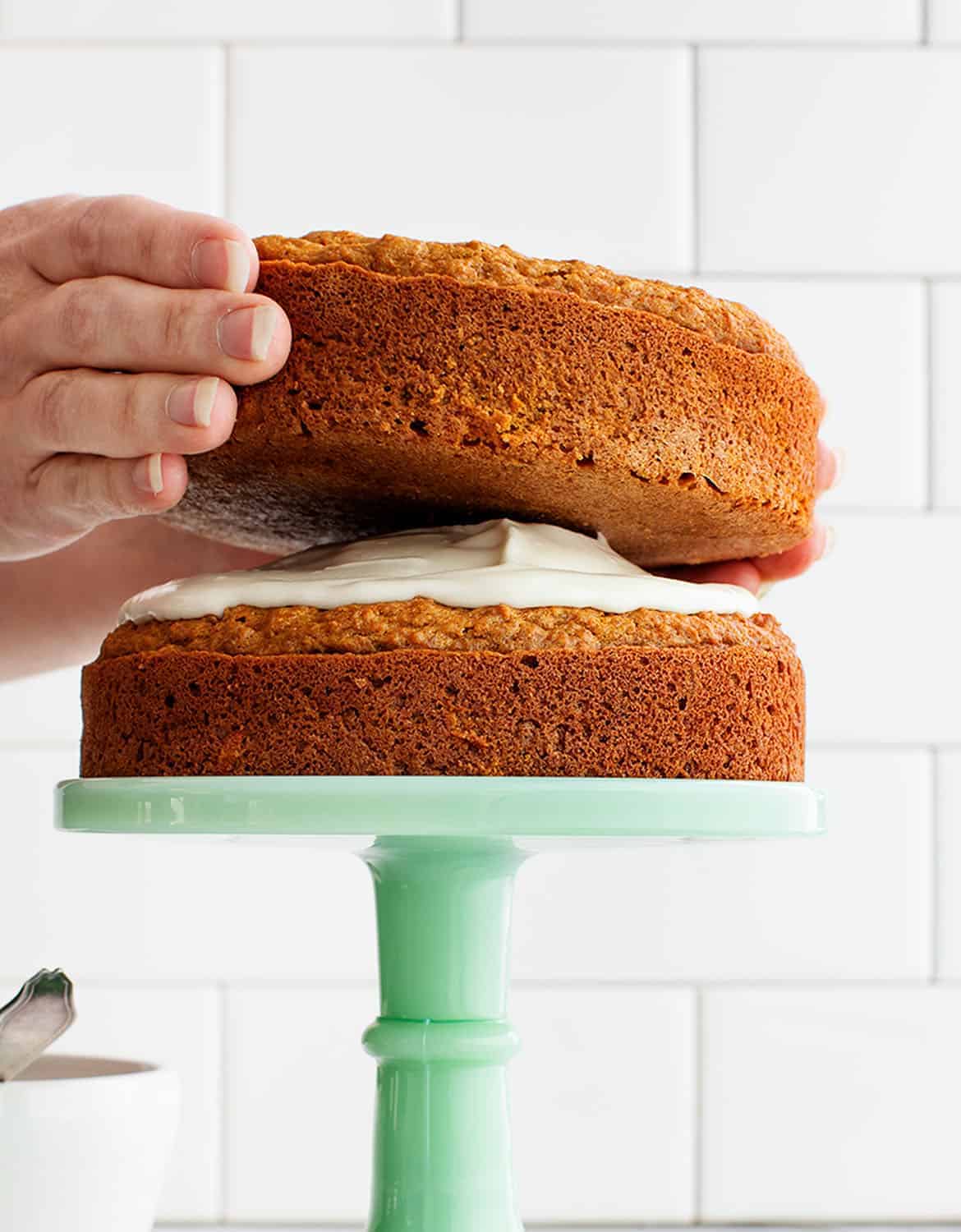 Hands placing a carrot cake over a green cake stand - Love & Lemons