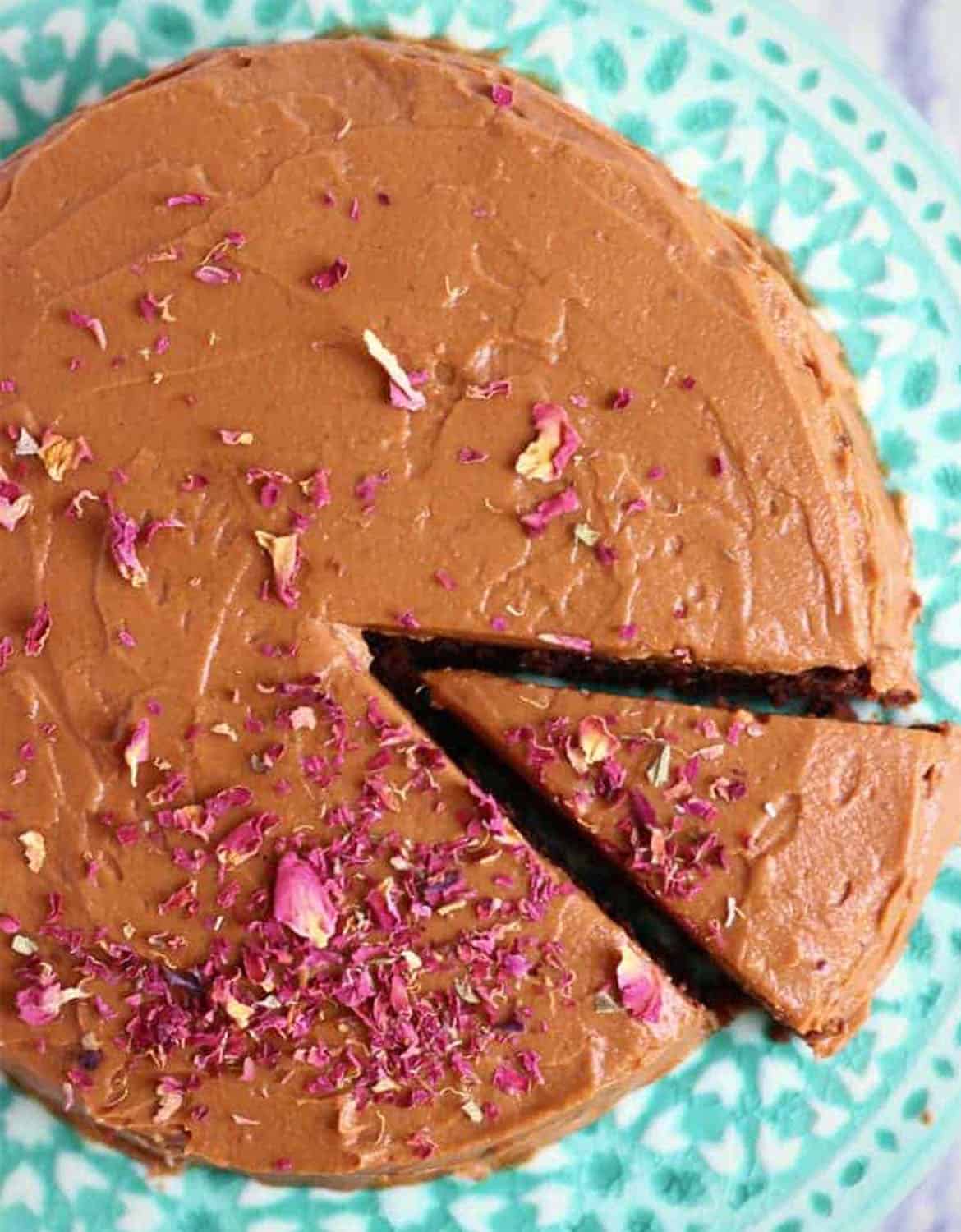 A round chocolate cake with some rose petals on top over a light green plate - Rhian's Recipes